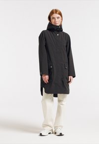 Svart lång kappa med huva, med en framtida dragkedja, två sidofickor och tryckknappsstängning. Tillverkad av lätt, matt tyg.