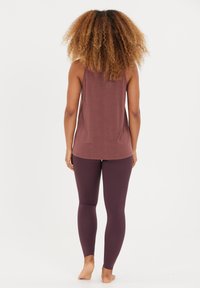 Top deportivo de color burdeos con un corte holgado, combinado con leggings morados. El top tiene una textura suave y un dobladillo redondeado.