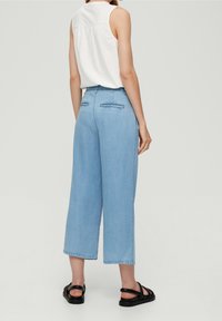 Light blue wide-leg jeans with a high waist, featuring back pockets and a smooth denim texture, paired with a white sleeveless top.