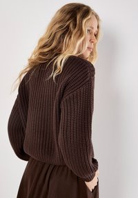 Brauner gestrickter Pullover mit einem strukturierten, gerippten Design und übersize Ärmeln, kombiniert mit einem passenden braunen Rock.