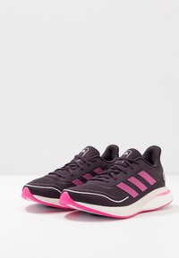 Černé a růžové sportovní boty s texturovaným svrškem, třemi růžovými pruhy, bílou mezipodešví a růžovou podešví.