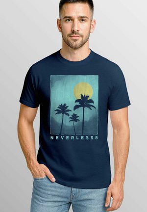 Ein mann mit einem bart trägt ein navy-blaues t-shirt mit palmensymbol und einem sonnenuntergangsdesign, mit "NEVERLESS" darunter gedruckt. Der Hintergrund ist hellgrau.