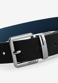 Ceinture en cuir noir avec une finition brillante, dotée d'une boucle en métal argenté et de l'inscription "NEXT" estampillée sur la boucle.