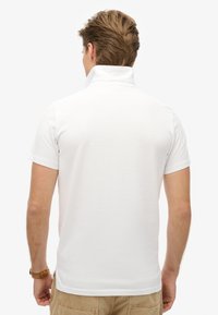 Biała koszulka polo z kołnierzykiem stojącym i krótkimi rękawami. Miękka tkanina o gładkiej fakturze. Minimalistyczny design, brak widocznych wzorów.