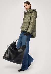 Vadderad jacka i olivgrönt, denimjeans och svart läderhandväska. Väskan har en slapp form och en enkel axelrem.