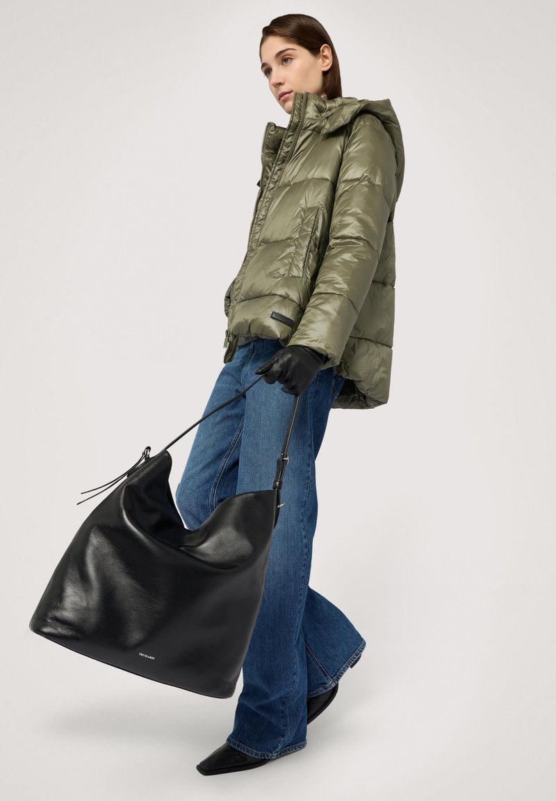 Vadderad jacka i olivgrönt, denimjeans och svart läderhandväska. Väskan har en slapp form och en enkel axelrem.