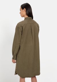 Olivengrünes, langärmliges Kleid mit lockerer Passform, Knopfmanschetten, Rückenfalte und abgerundetem Saum. Aus leichtem Stoff gefertigt.