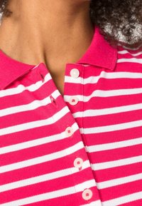 Rosa och vit randig polo skjorta med krage, med sju knappar fram, tillverkad av stickad material.