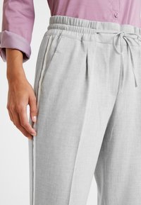 Light gray elastic waist pants with drawstring, featuring side pockets and a contrasting white stripe along the outer seam, textured fabric.