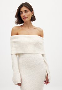 Õlavarrelt kukkuv kreemivärvi kudum dresses ribatekstuuriga, pikad varrukad ja külgmised lõhikud. Pehme materjal ning istuv siluett.