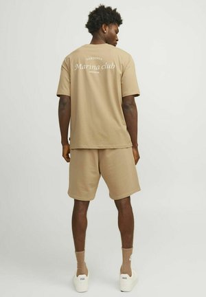 Beige bomulds t-shirt og shorts sæt. T-shirten har hvid tekst "Sardinia Marina club" på ryggen. Enkel design, afslappet pasform.