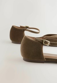 Brązowe aksamitem baleriny z zaokrąglonym noskiem, regulowanym paskiem na kostkę i złotą klamrą. Teksturowana powierzchnia i niski obcas.