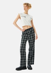 Top corto blanco con estampado "Los Ángeles 96", combinado con pantalones de cuadros en blanco y negro de cintura alta. Botas de plataforma negras y gruesas.