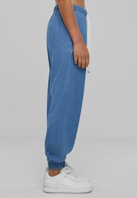 Pantalones jogger de denim azul claro con cintura elástica y cordón blanco, con puños ajustados y bolsillos laterales. Llevados con zapatillas blancas.