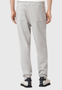 Lichtgrijze joggingsbroek met een relaxed fit, voorzien van elastische boorden, twee achterzakken en een zachte textuur. Draag met zwart-witte sneakers.