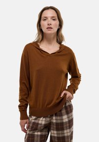 Pull à capuche marron avec poignets et ourlet côtelés, en tissu doux et coupe décontractée, associé à un pantalon à motif écossais dans des tons neutres.
