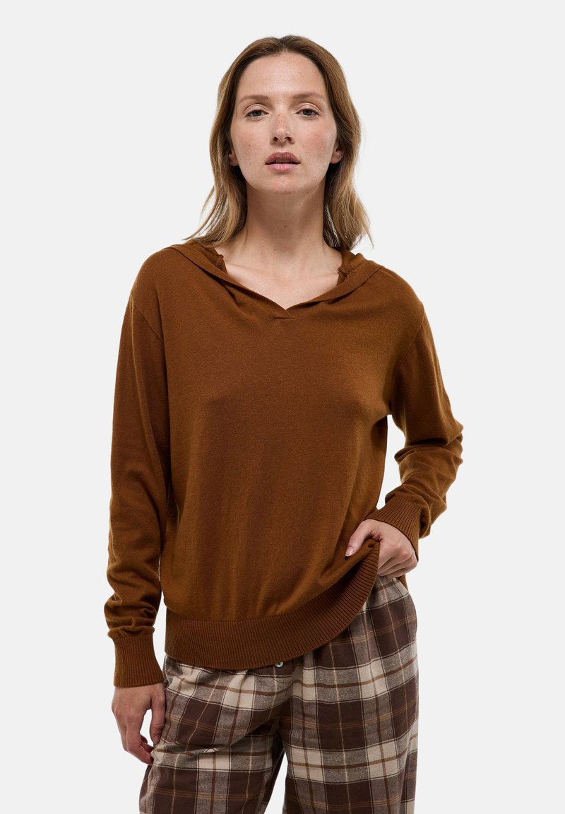 Pull à capuche marron avec poignets et ourlet côtelés, en tissu doux et coupe décontractée, associé à un pantalon à motif écossais dans des tons neutres.