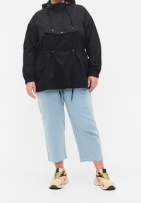 Svart huvjacka med dragsko och frontficka, tillsammans med ljusblå avklippta jeans och beige sneakers med mörka detaljer.