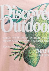 Text "Discover Outdoors" vyrazený na ilustrácii zelenej zelene na ružovej látke s menším bielym potlačeným textom o dizajne a pohodlí.