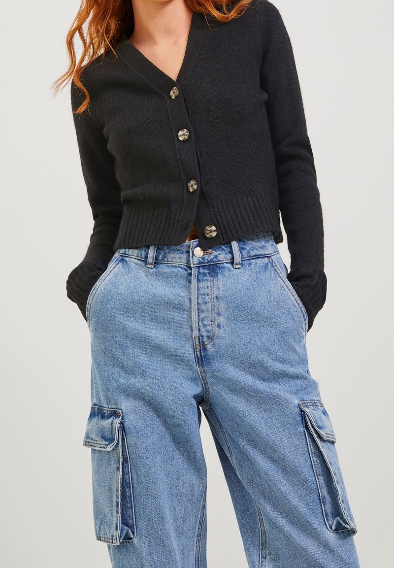 Cardigan nero a coste con scollatura a V e chiusura a cinque bottoni, abbinato a jeans cargo blu chiaro con tasche laterali.