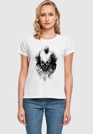 T-shirt en coton blanc avec un design graphique noir ressemblant à un visage de clown avec des motifs de vagues sonores ; manches courtes et coupe décontractée.