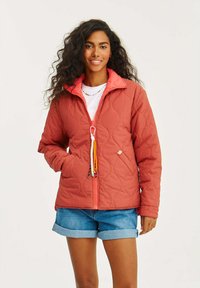 Nadmuchany, rdzawy kurtka z koralowym wewnętrznym kołnierzem, z zapięciem na zamek błyskawiczny z przodu, dwoma bocznymi kieszeniami i kolorowymi akcentami w postaci sznurków.