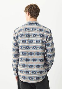 Langarmhemd mit einem geometrischen Muster in Blau, Beige und Orange. Hergestellt aus gewebtem Stoff mit geradem Schnitt und geknöpften Manschetten.