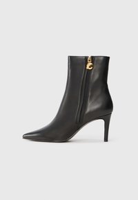 Bottine noire en cuir avec un bout pointu, un talon haut élancé et une fermeture éclair sur le côté, arborant une touche dorée au tirette de la fermeture.