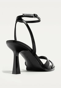 Schwarze High-Heel-Sandalen mit eleganten Lederriemen, einer verstellbaren Schnalle am Knöchel und einem quadratisch geformten Absatz für Stabilität.