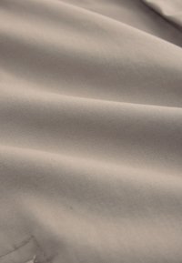 Primer plano de tela beige que muestra pliegues suaves y textura fina tejida.