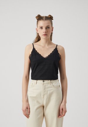 Svart cami med bølget blonderkant, med tynne stropper og teksturert stoff, kombinert med høyhalkede kremfargede denimbukser.