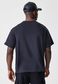 Čierne tričko s krátkym rukávom a voľným strihom, vyrobené z bavlny. Obsahuje rovný lem a žiadne viditeľné dizajnové prvky.