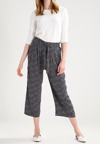 Czarno-białe spodnie w kratkę o skróconym kroju, luźnym fasonie, z elastycznym pasem i subtelnymi fałdami, zestawione z białą, teksturowaną bluzką.