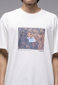 T-shirt blanc à manches courtes avec un imprimé rectangulaire de fleurs sur fond marron. Le texte en bas indique "FORMER."