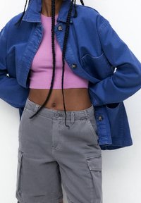 Niebieska kurtka dżinsowa z dwoma kieszeniami na piersiach, zestawiona z różowym krótkim topem i szarymi spodniami cargo z bocznymi kieszeniami i luźnym krojem.