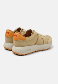 Light beige sneakers with textured canvas upper, orange accents, and white laces. Chunky sole with orange tread for grip, brand logo on heel.