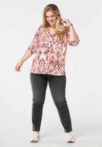 Lichte, gestreepte blouse in roze en crème tinten met driekwart mouwen en een ronde halslijn, gecombineerd met donkergrijze broeken.