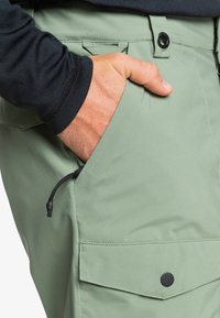 Lichtgroene cargo pants met een zijzak met trekkoordsluiting, zwarte knoopaccenten en een gladde, gemengde stof.