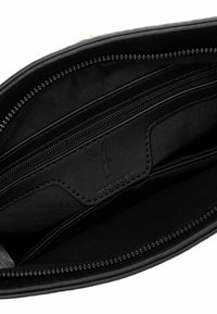 Černý vnitřek tašky zobrazující několik přihrádek na zip a koženou značkovou nášivku s detailním prošíváním.