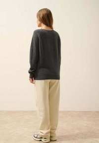 Szary sweter z dzianiny z okrągłym dekoltem, zestawiony z kremowymi spodniami dresowymi i szarymi trampkami. Gładka faktura z delikatnym prążkowaniem na mankietach.