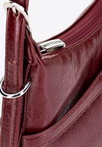 Bordowa skórzana torba na ramię o gładkiej fakturze, ze srebrnymi akcentami i zapięciem na zamek. Posiada detal z logo oraz kieszonkę zewnętrzną.