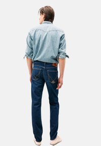 Jeans di denim blu scuro, design a gamba dritta con cuciture dettagliate. Abbinati a una camicia di denim azzurro, con maniche arrotolate.