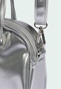 Srebrna metaliczna torba na ramię o błyszczącej fakturze, z suwakiem, srebrnymi elementami metalowymi i odpinanym paskiem. Minimalistyczny design.