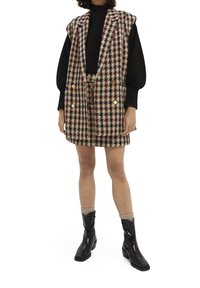 Tweed-Weste mit schottischem Muster in Maroon, Creme und Marineblau, mit goldenen Knöpfen, getragen über einem schwarzen Oberteil, kombiniert mit knieb hohen schwarzen Stiefeln.