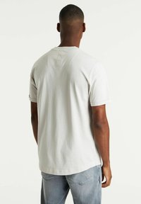 T-shirt in cotone grigio chiaro con scollatura rotonda, maniche corte e dettaglio a toppa sulla parte superiore della schiena, abbinato a jeans blu sbiaditi.