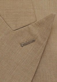 Tessuto marrone caratterizzato da una trama liscia con un taglio diagonale e un piccolo dettaglio di cucitura decorativa visibile. Il design è minimalista.