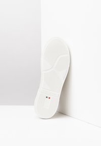 Biała podeszwa sneakersów z teksturowanej gumy dla lepszej przyczepności, z wytłoczonym logo i szczegółem w kolorach flagi włoskiej. Gładkie krawędzie i minimalistyczny design.