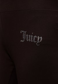 Κοντινό πλάνο σκούρου υφάσματος με τη λέξη "Juicy" γραμμένη με μικρές λαμπερές στρας.