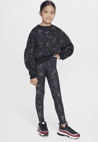 Felpa nera e leggings con motivo di spruzzi bianchi. Le scarpe da ginnastica presentano un design in nero, rosso e bianco. Forme semplici e arrotondate in tutto.