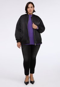 Mustat bomber-takit vetoketjulla ja sivutaskuilla, puettuna päälle violetti villapaita. Mustat kuluneet skinny-farkut ja mustat teräväkärkiset korkokengät.